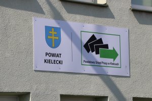 Ściana budynku urzędu z tablicą z herbem powiatu kieleckiego i logiem Powiatowego Urzędu Pracy w Kielcach 